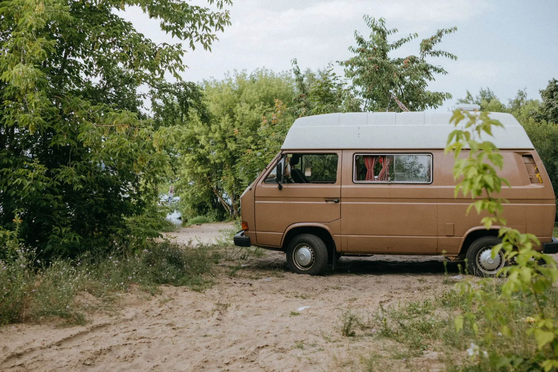 A camper van parked among trees at a wooded campsite, the kind of site a portable water heater program ships to