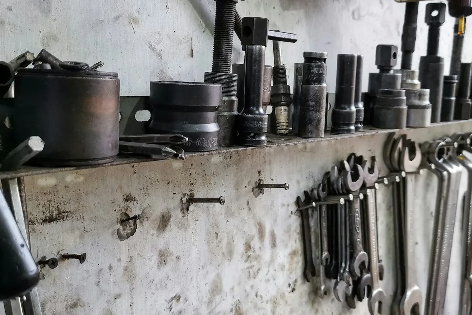 A workshop tool wall above a bench, spanners and sockets racked in the order a repairer reaches for them