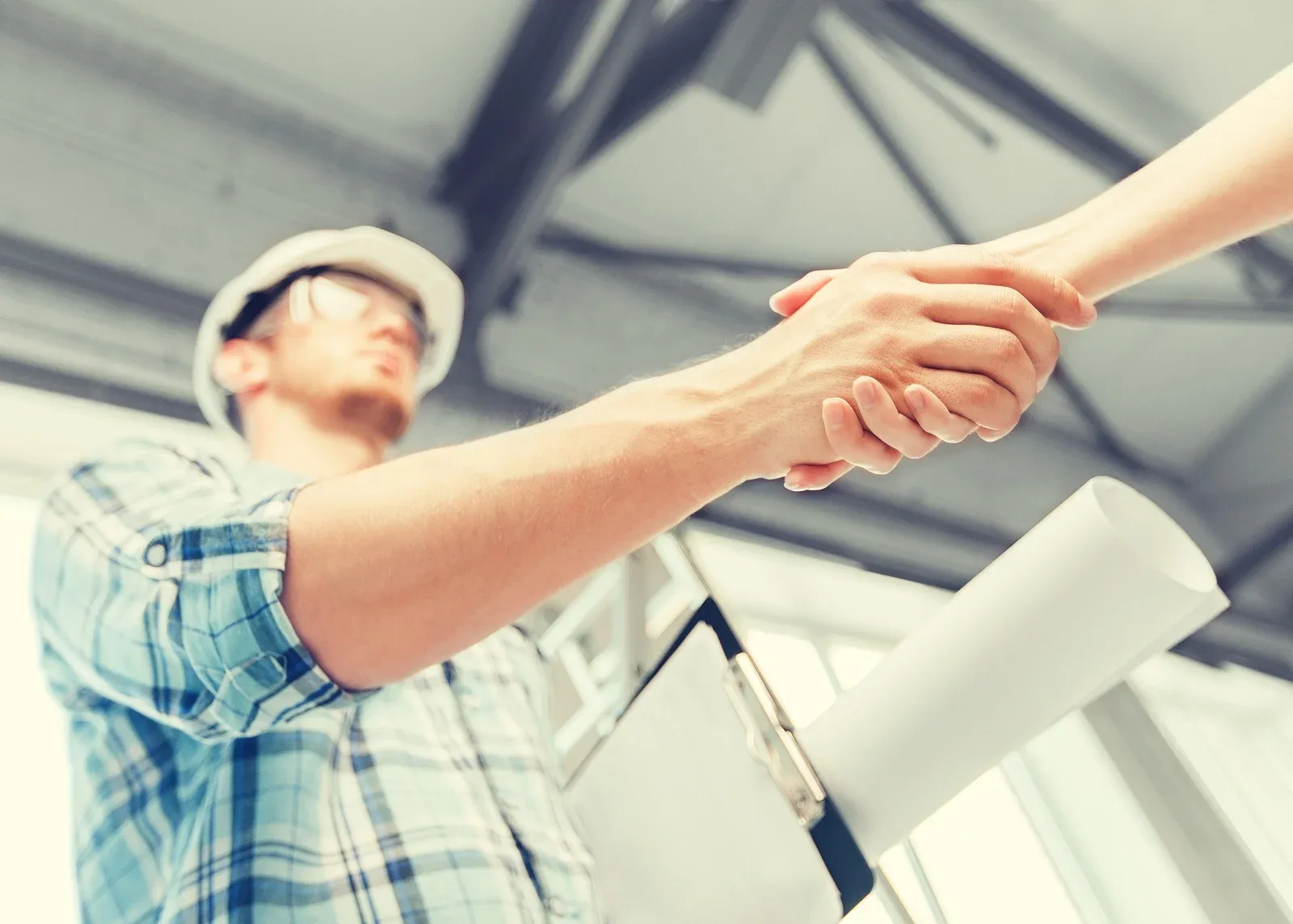 Two people shaking hands under the steel roof trusses of a workshop, an approved outside process agreed in writing