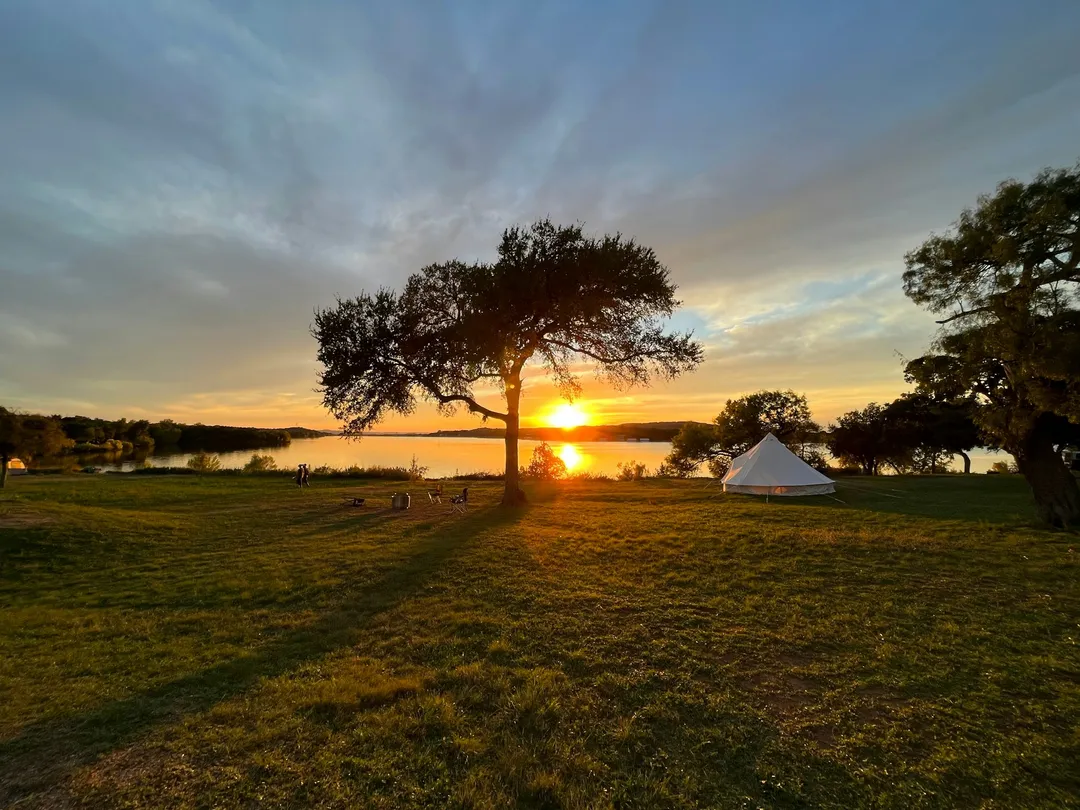 Tent pitched on grass beside a lake at sunset, the scene the camping build is sold into