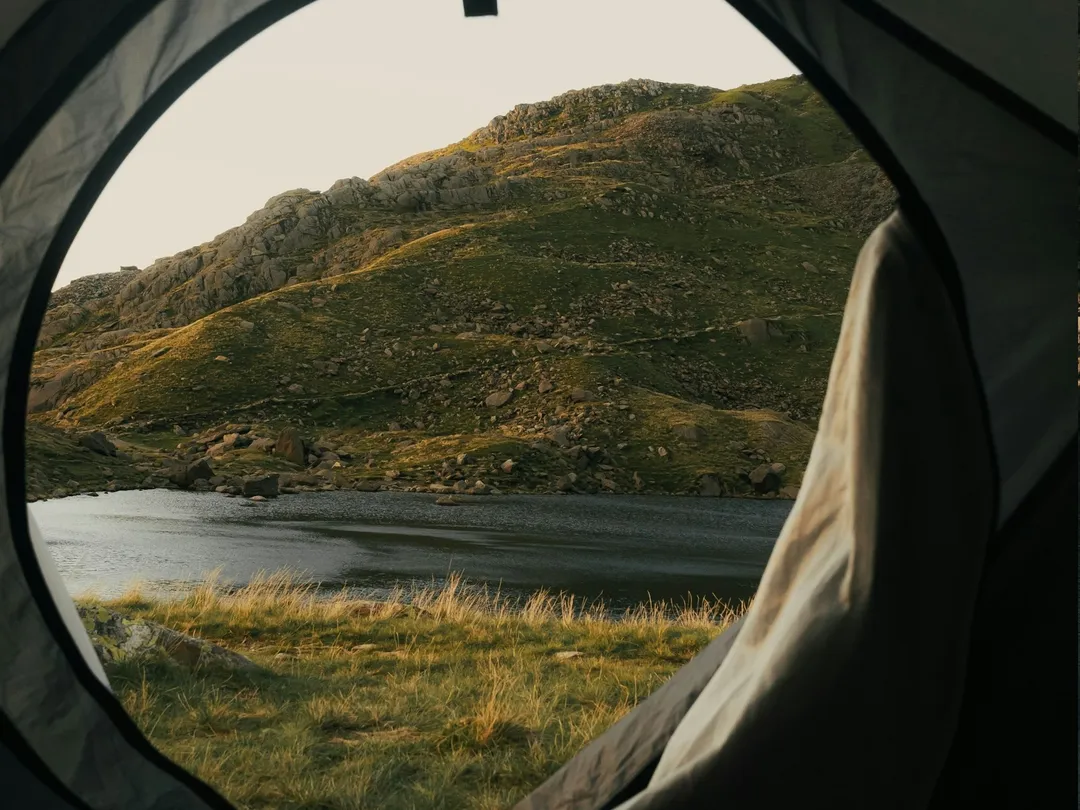 View from inside a tent towards a mountain lake at first light