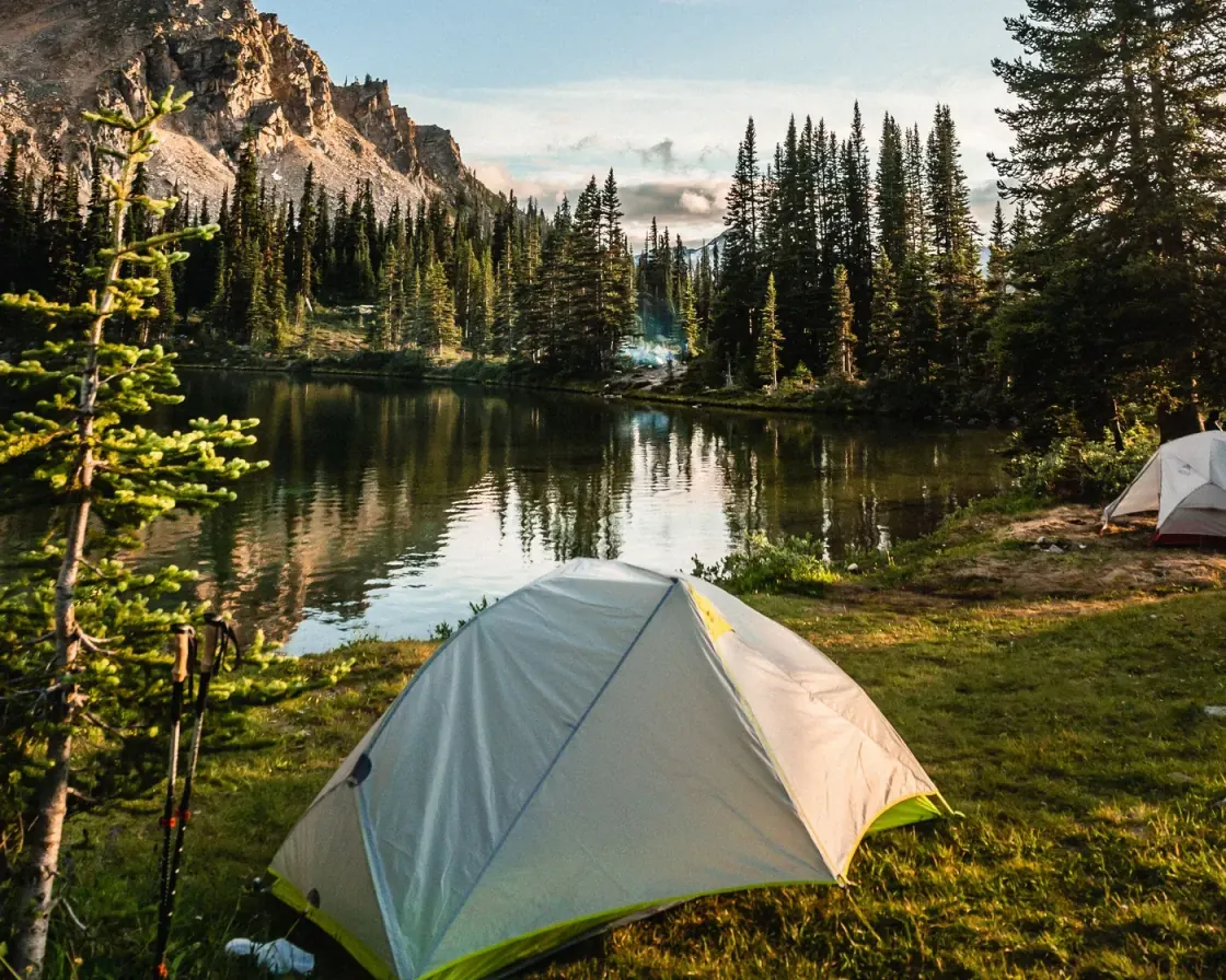 A tent pitched on a grassy bank beside a mountain lake at a forest campsite