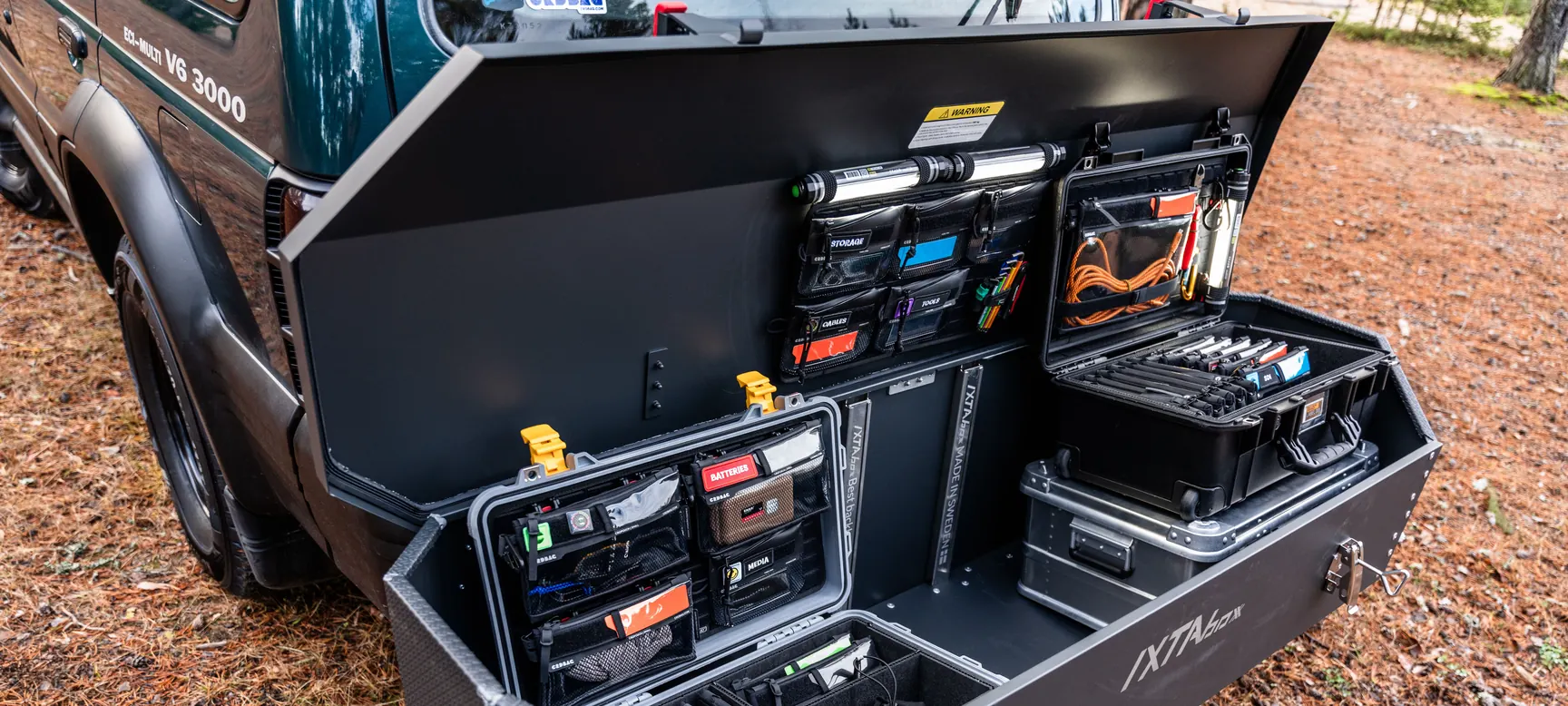 An open vehicle storage drawer holding organised equipment cases and compartments at a camp