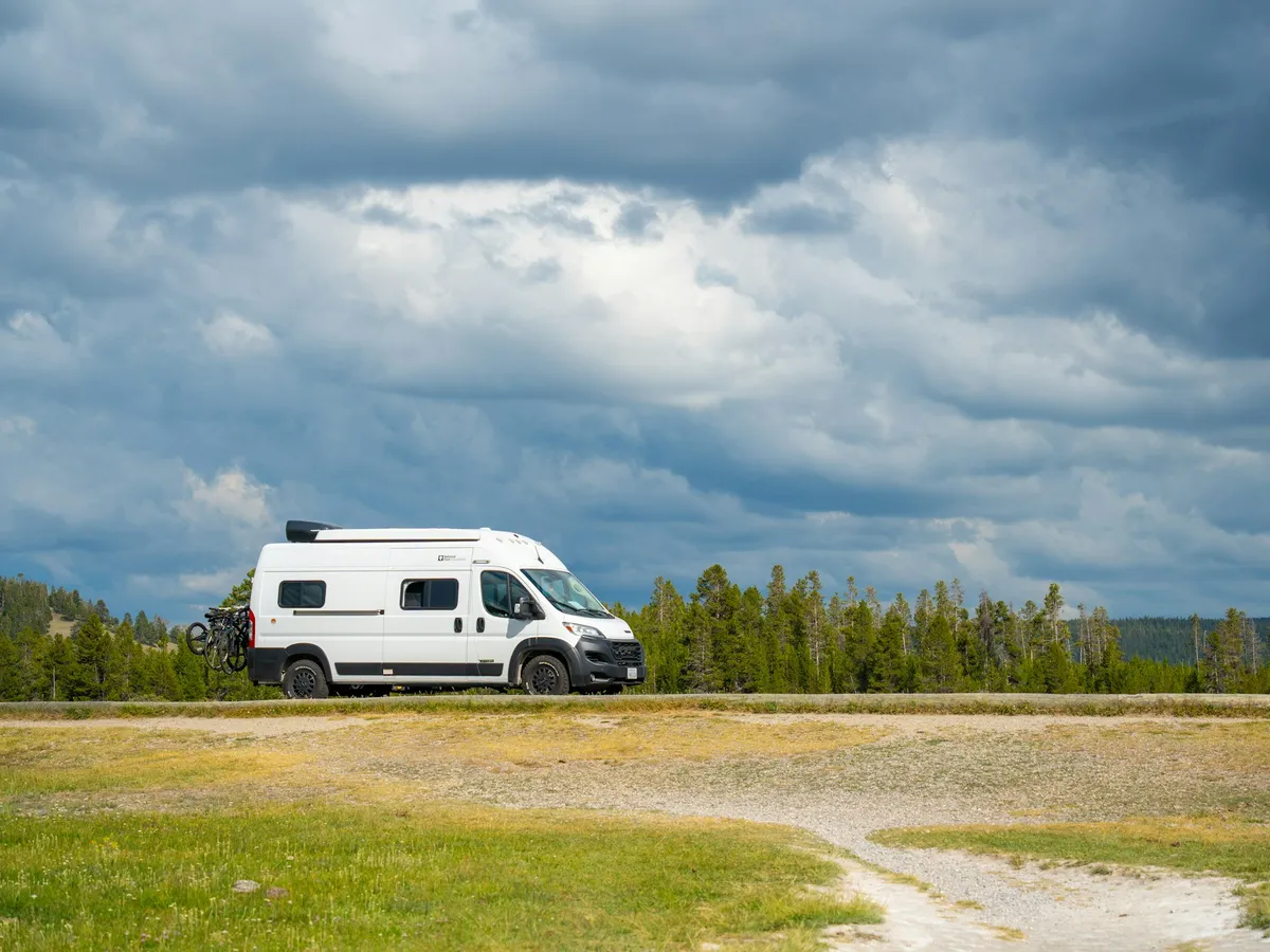 A white camper van parked on a gravel clearing under a wide cloudy sky