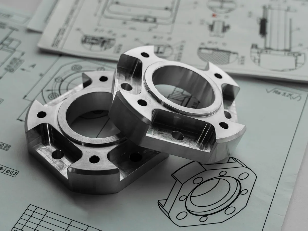 Machined metal components resting on a technical drawing at a drafting bench