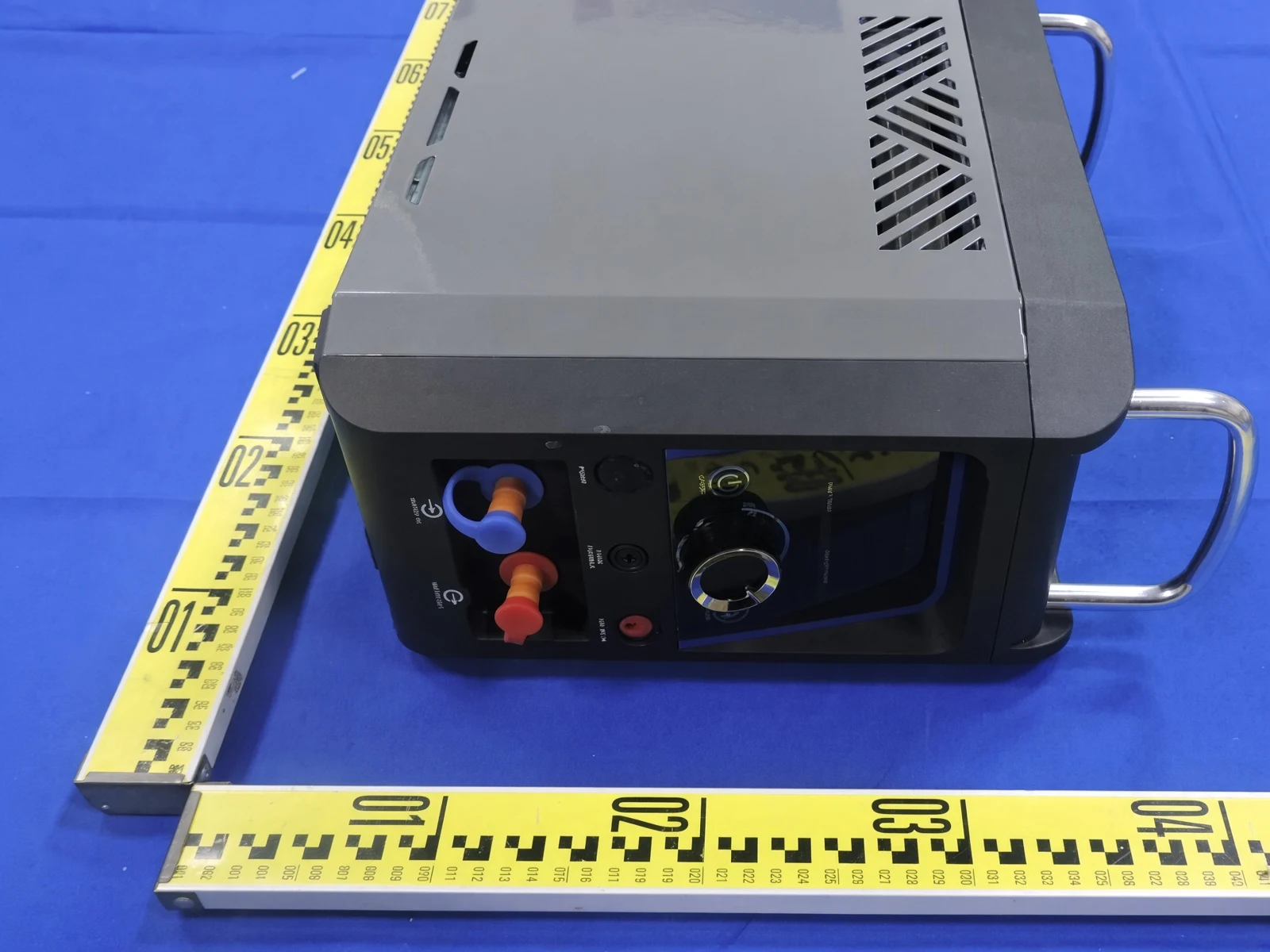 A portable water heater photographed on the laboratory bench, showing its control panel, water connections and lifting handle beside a steel rule