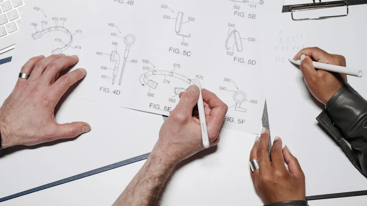 Hands sketching a technical drawing beside a laptop on a work desk