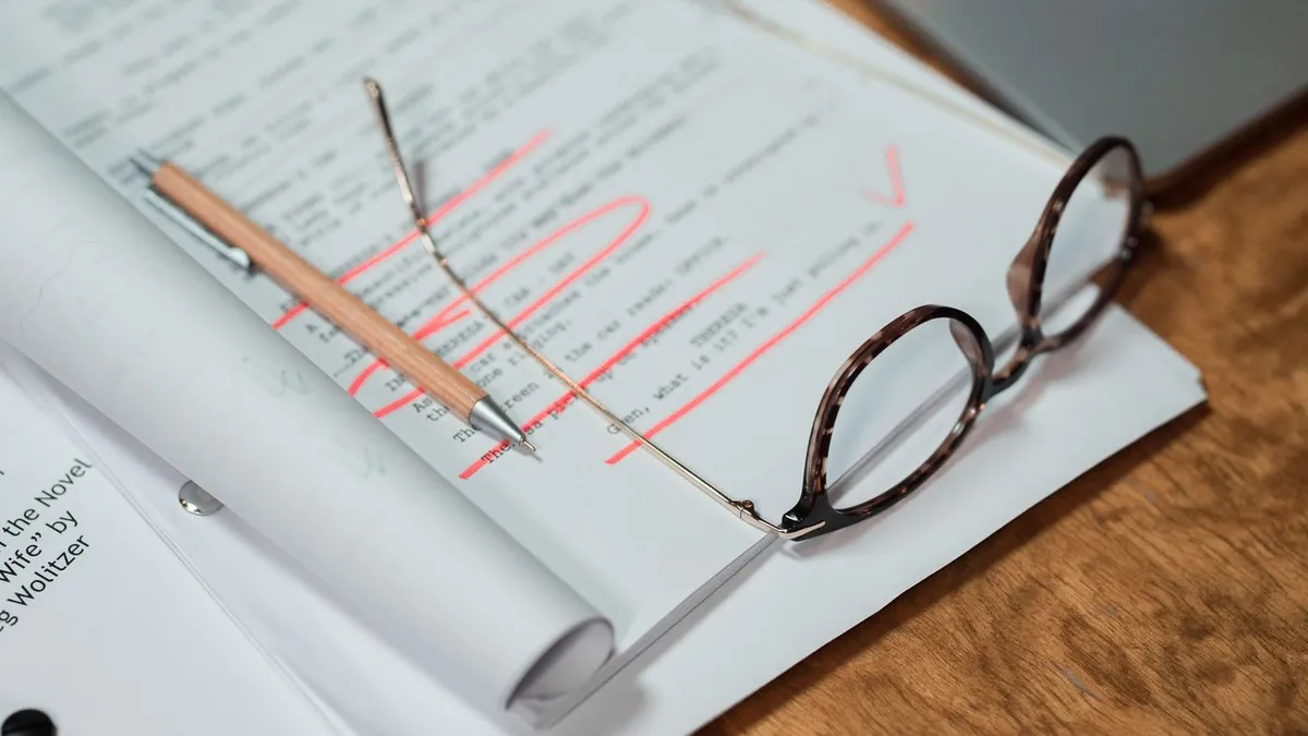 Annotated specification documents, a pencil and glasses on a desk beside a laptop