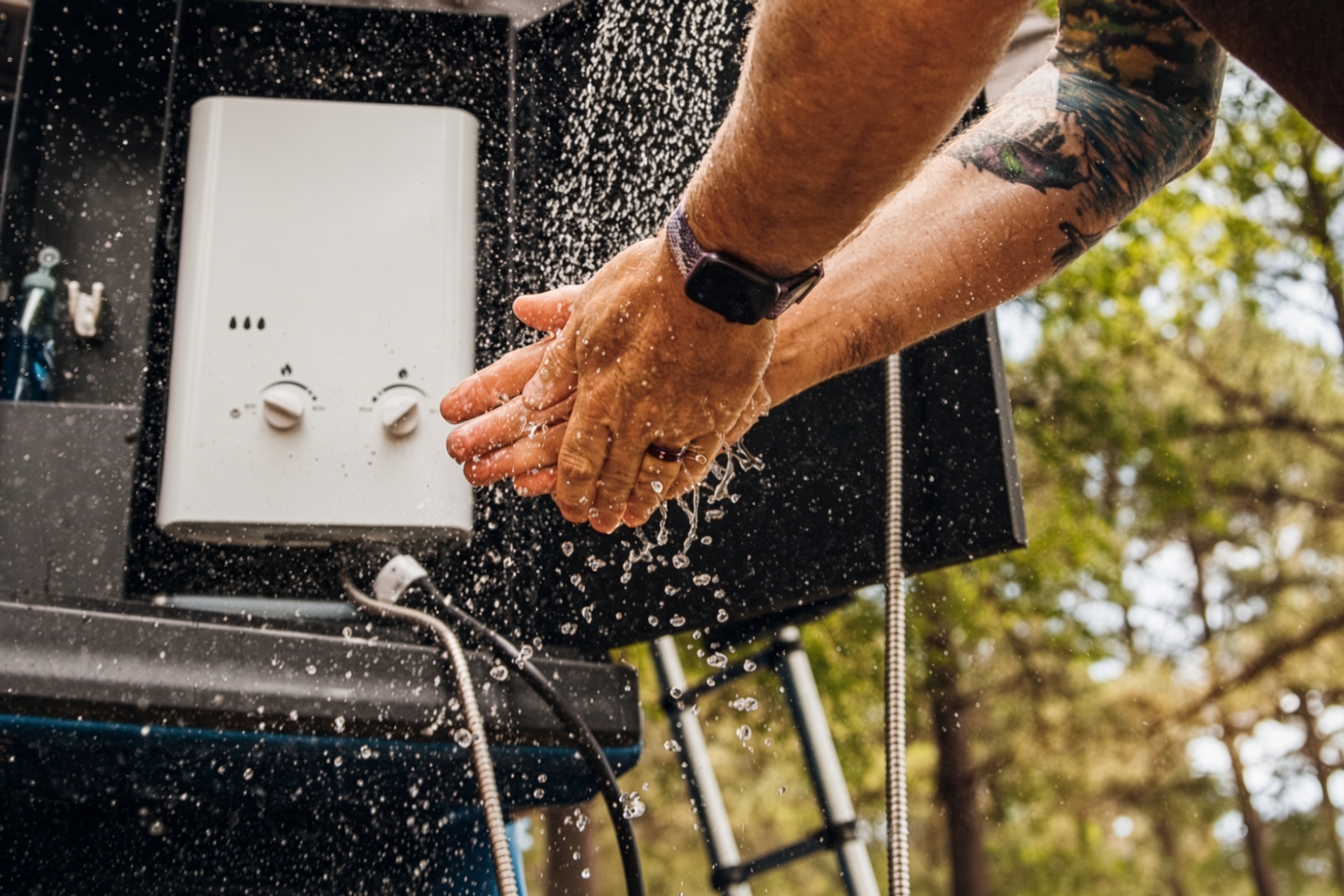 Hands rinsed under a Gulfstone portable water heater mounted on a truck