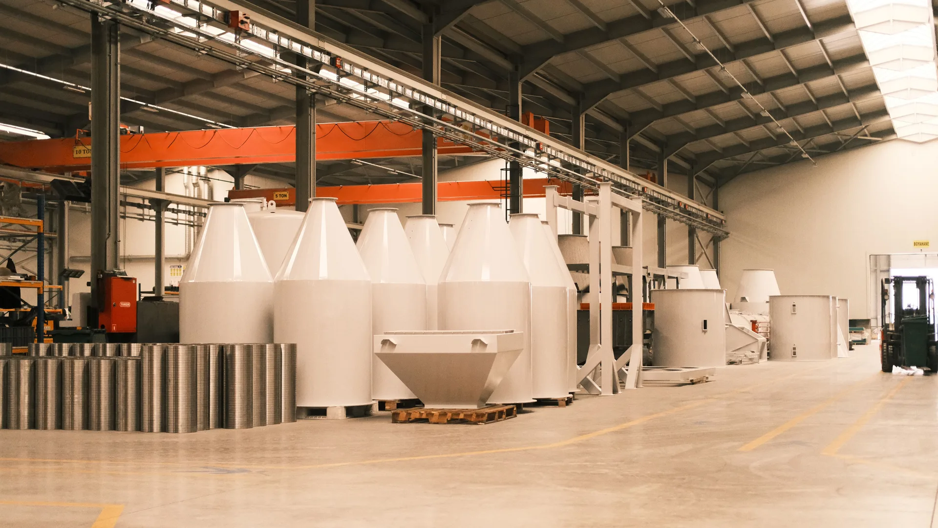 A bright production hall with large moulded components staged on pallets and overhead lifting rails