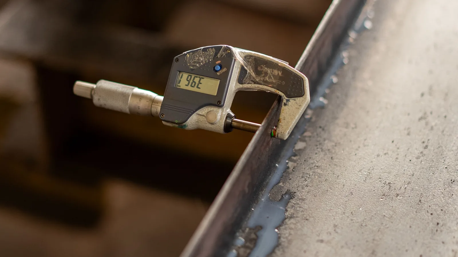 A digital micrometer measuring a machined steel edge