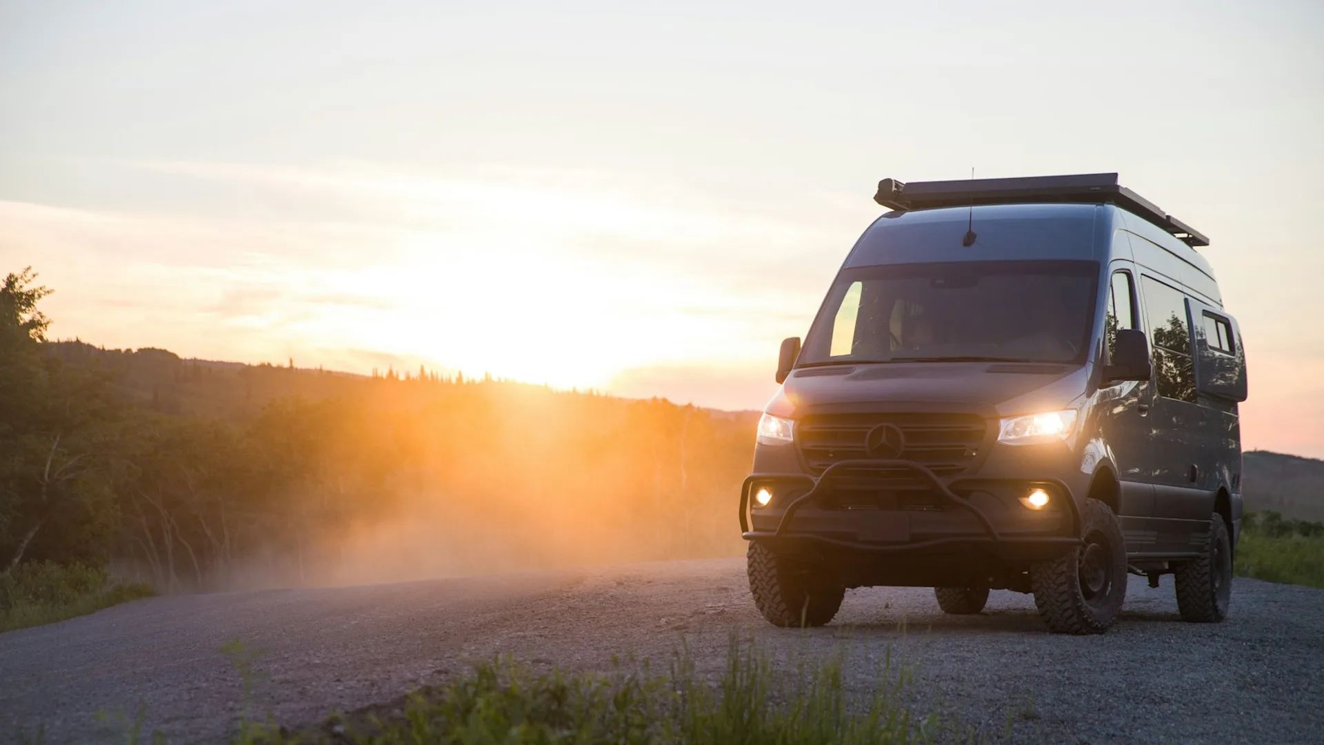 Overland camper van on a forest road at dusk with headlights on