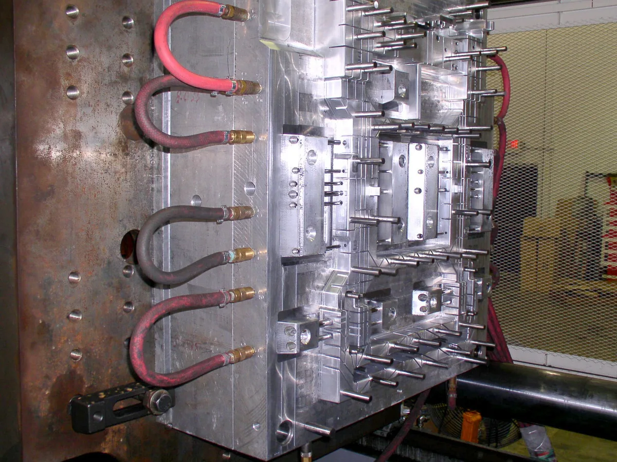 A polished steel injection mould with cooling lines, standing in a tooling shop