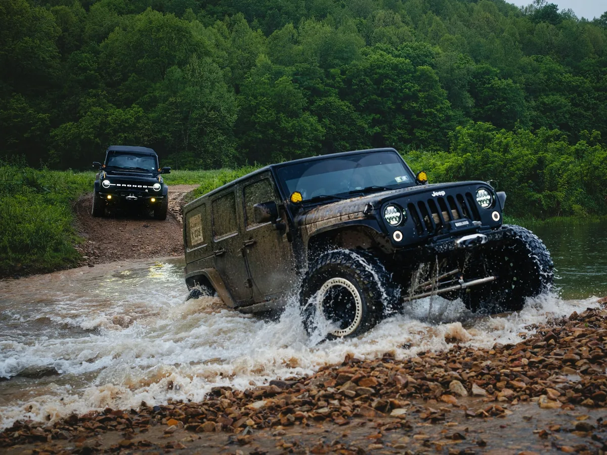 A four-wheel-drive vehicle crossing a shallow river on a remote track