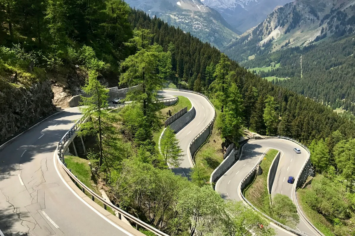 Hairpin bends on an alpine pass road through a forested mountain valley