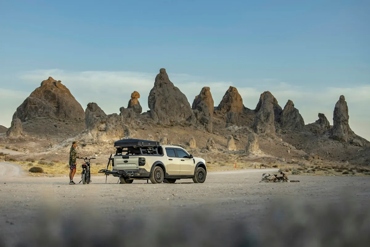 A pick-up with a roof tent and a motorcycle on the rear carrier below desert rock formations