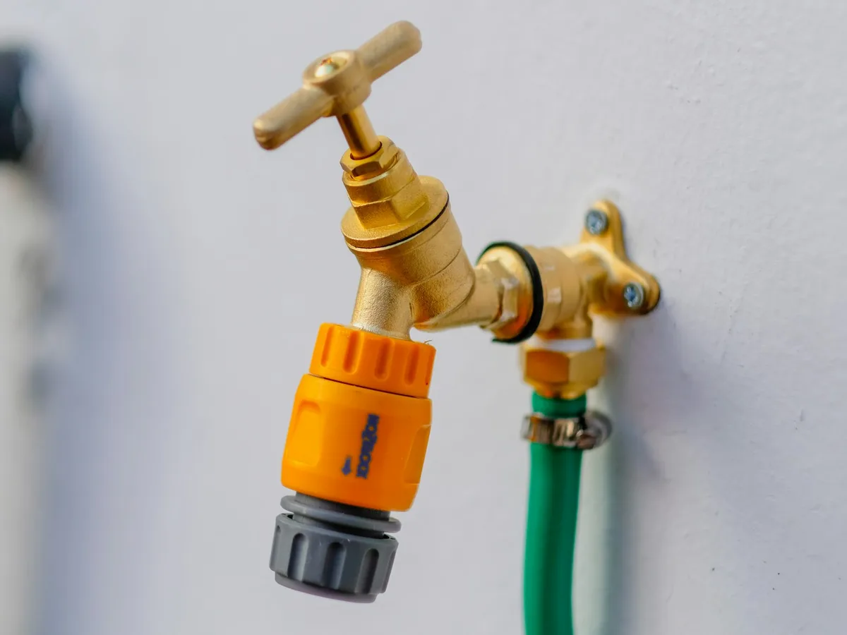 An outdoor tap on a wall with a hose connector, the kind of rinse point a pool surround is served from