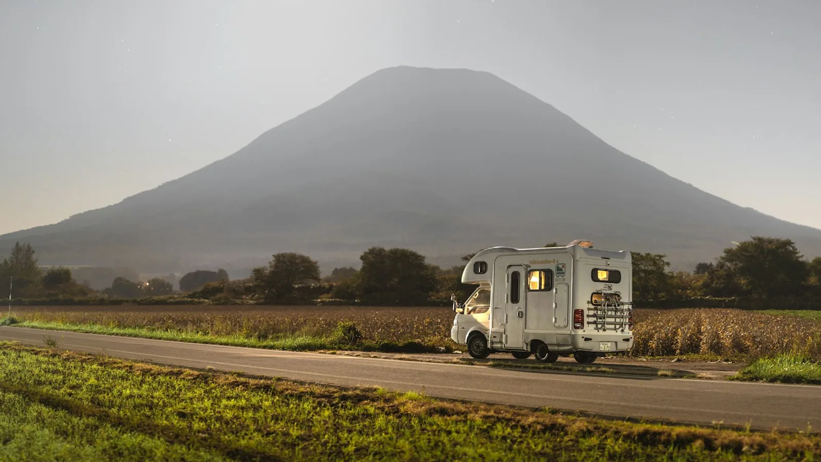 A camper parked on a road below a mountain, the vehicle a tankless water heater is built into