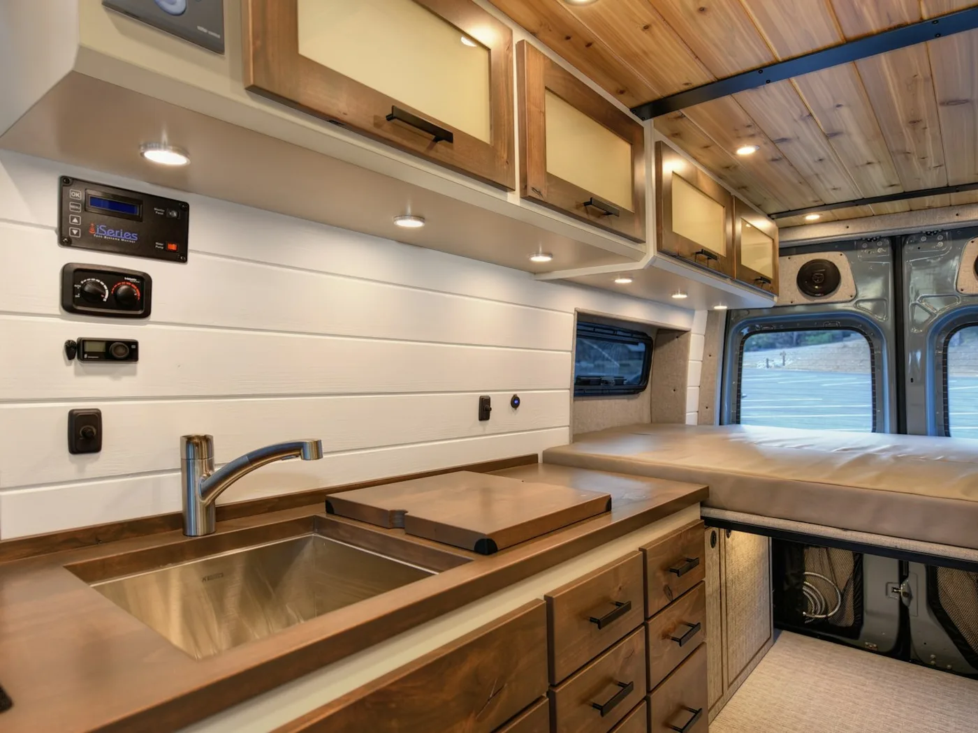 A camper galley with a sink, hob and overhead lockers running along one wall