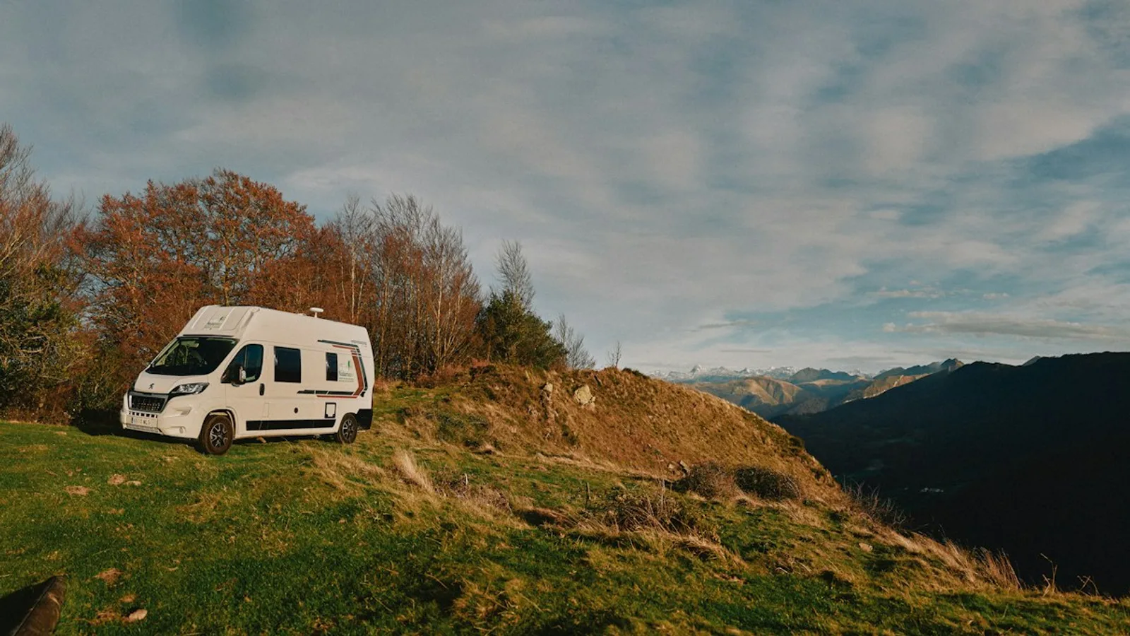A camper parked on a grassy hillside with a valley and mountains beyond