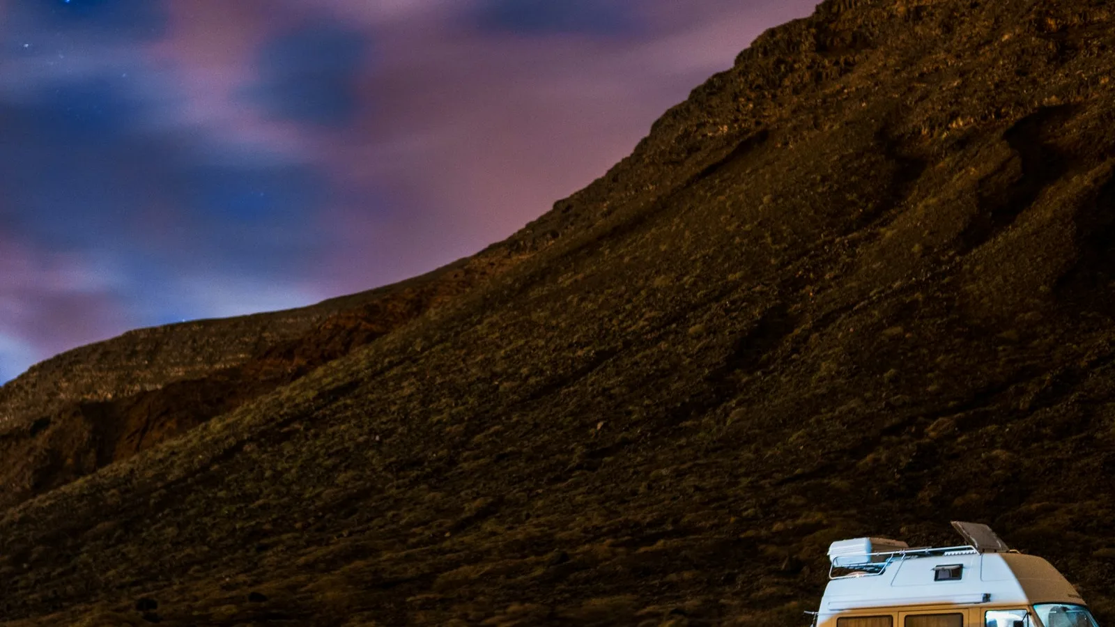 A camper parked at the base of a rocky mountain, mirrored in still water