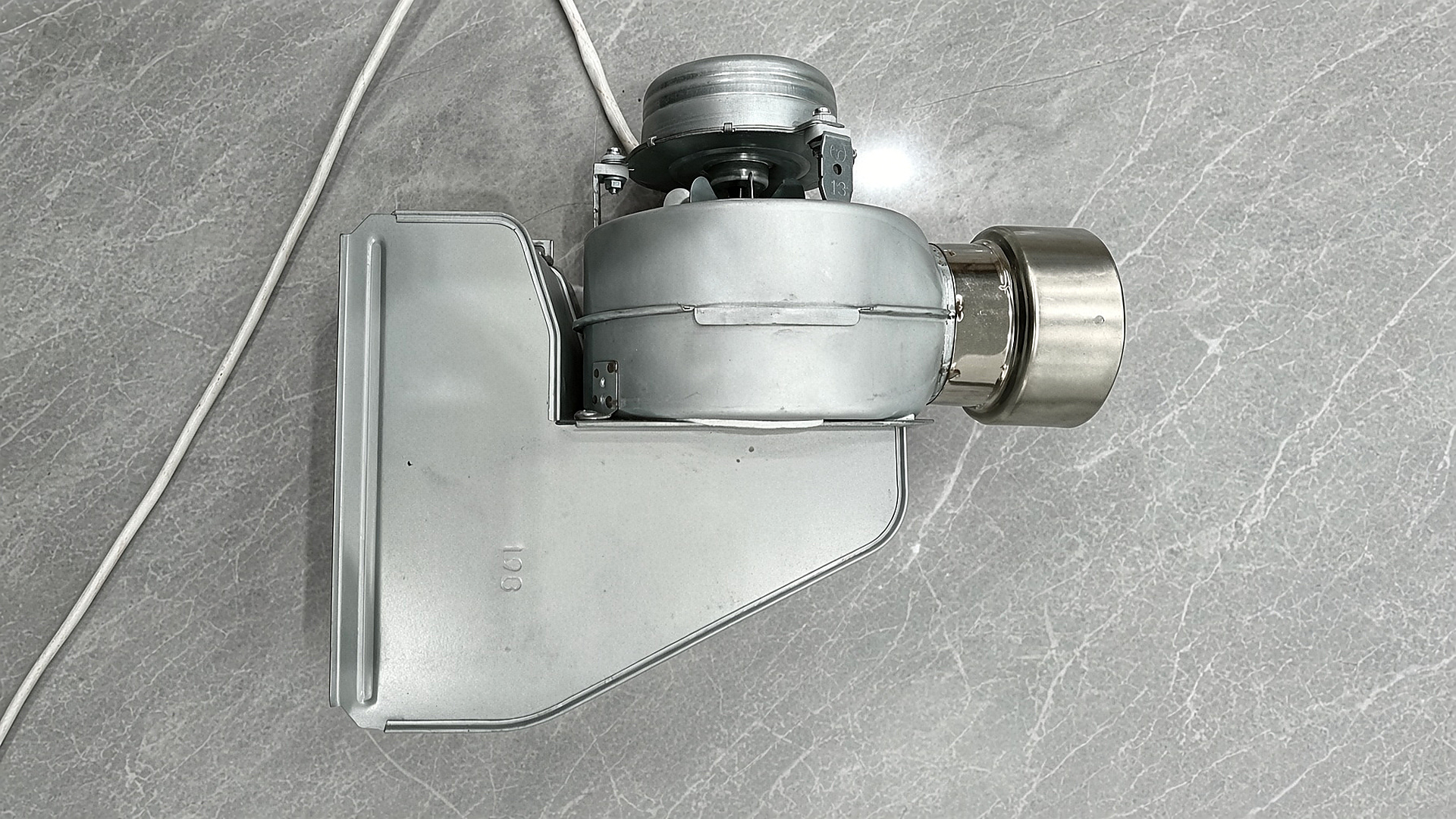 The Gulfstone RV water heater combustion fan: a sheet-metal scroll housing and motor with a cylindrical exhaust outlet and its mounting bracket
