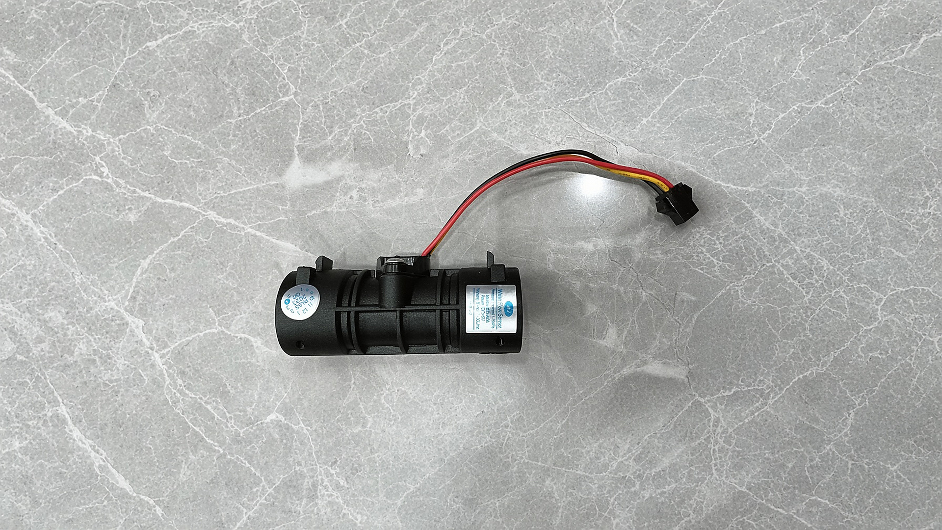 The Gulfstone RV water heater water-flow sensor: a black glass-filled nylon body with a three-wire harness and plug, on a grey ground